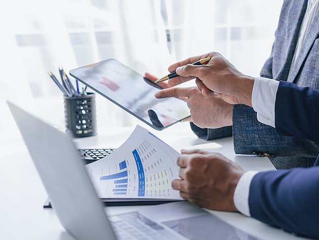 Zwei Personen arbeiten gemeinsam mit Diagrammen und einem iPad am Arbeitsplatz