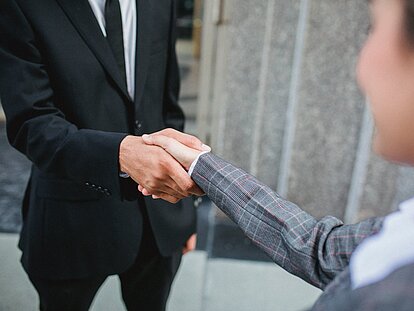 Zwei Personen in Anzügen geben sich die Hand